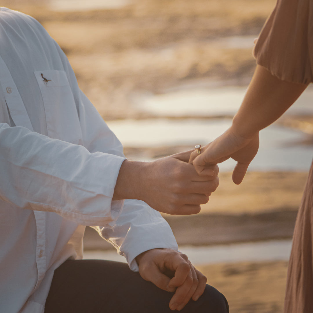 Two people holding hands after a proposal on a beach with a warm, golden glow.
