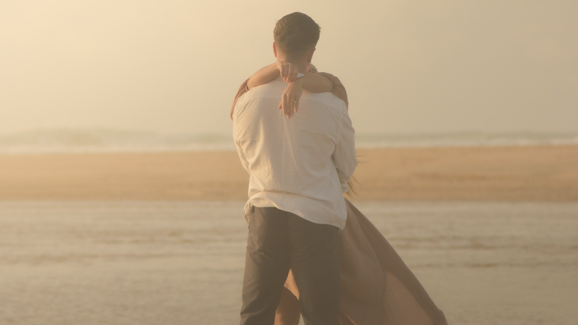 Two people embracing on a beach at sunset