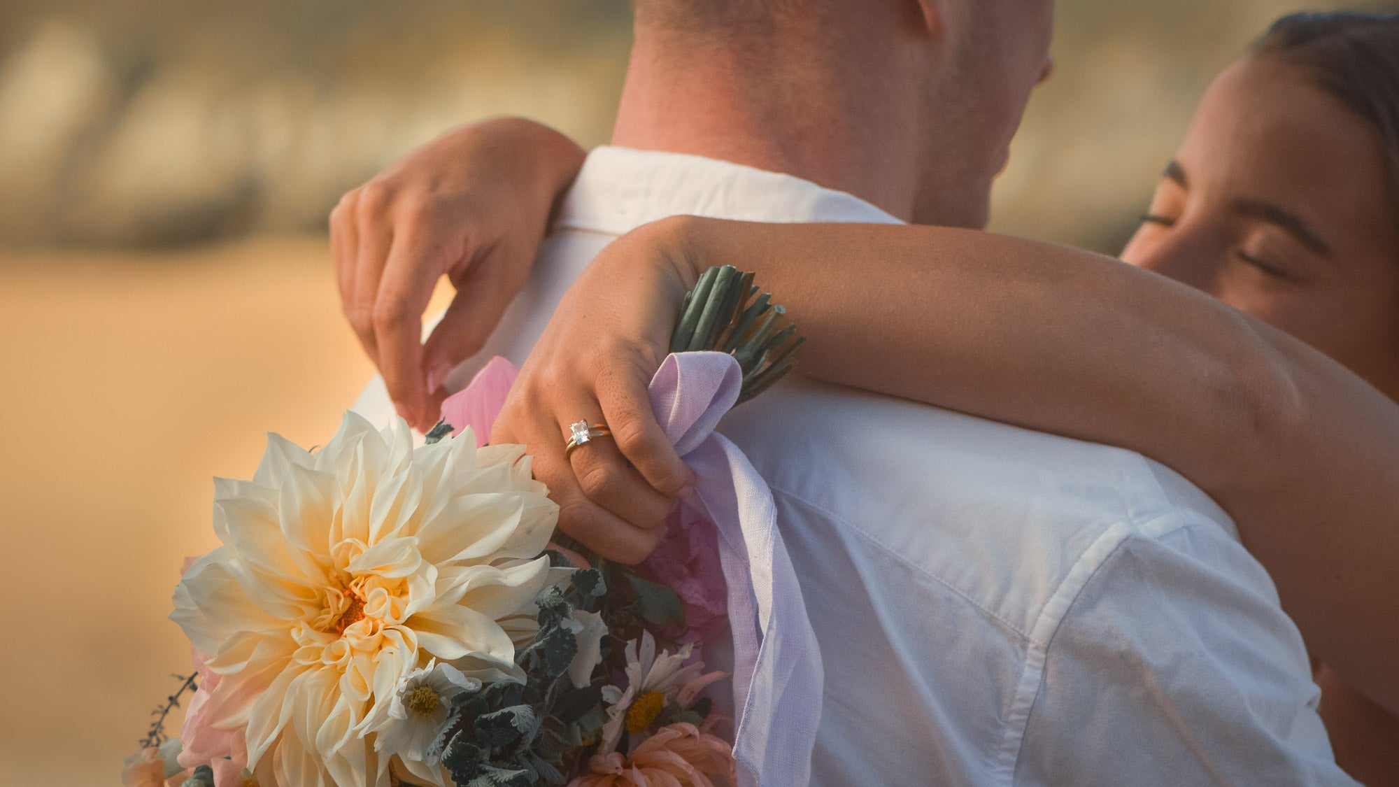 Person holding a bouquet of flowers with another person in a close embrace, possibly on a beach.