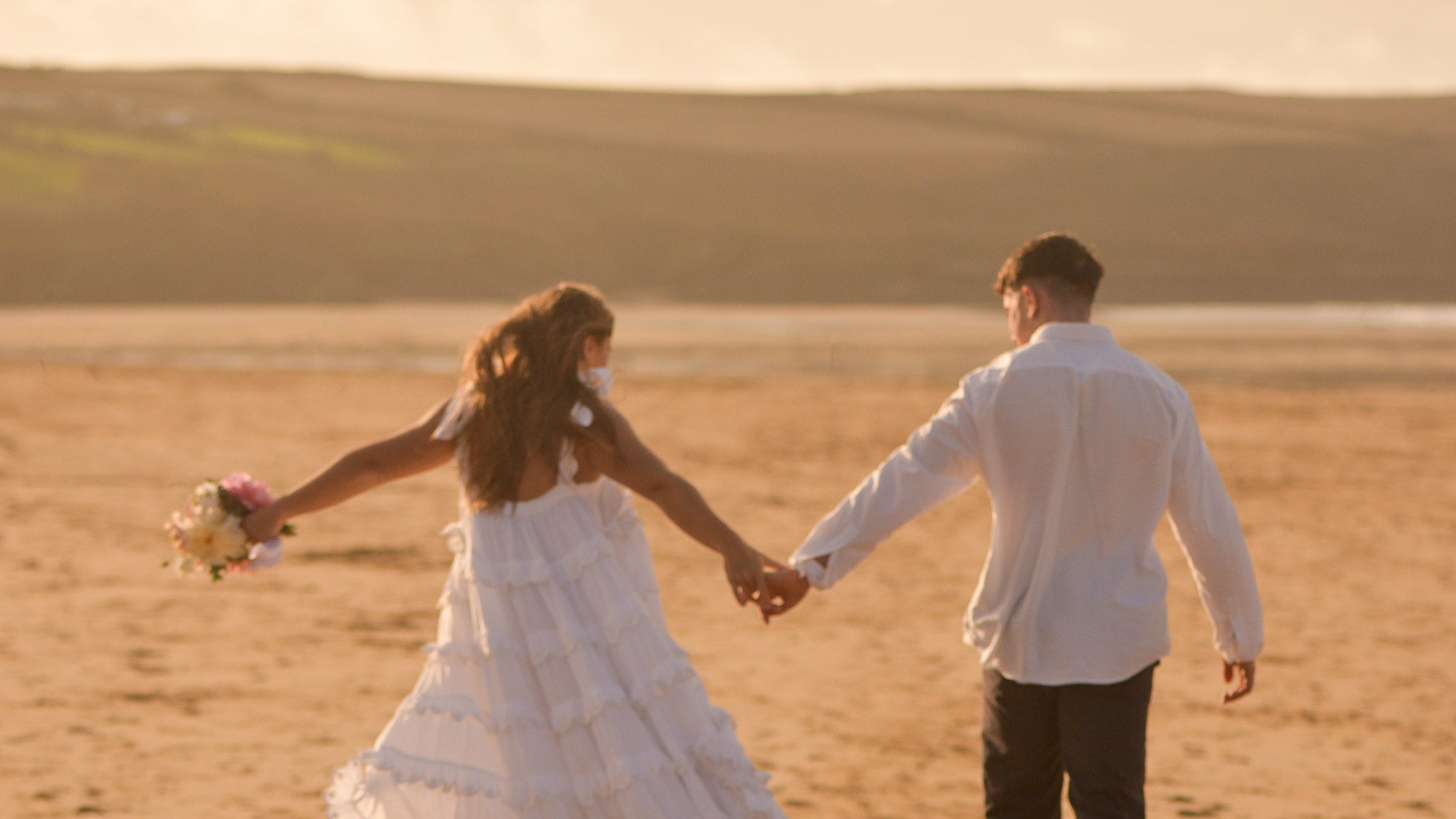 Bride and groom holding hands on a beach at sunset