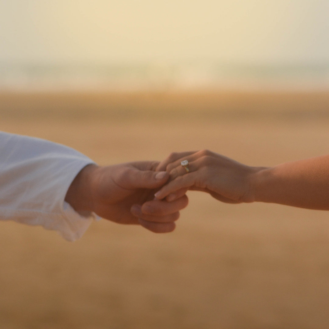 Two people holding hands with a blurred beach landscape in the background