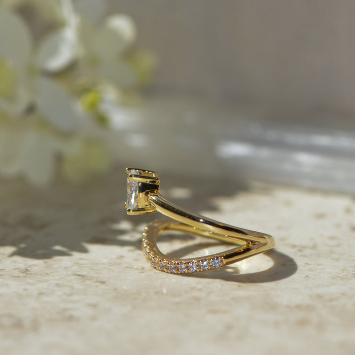 Gold ring with a diamond on a light surface with blurred flowers in the background