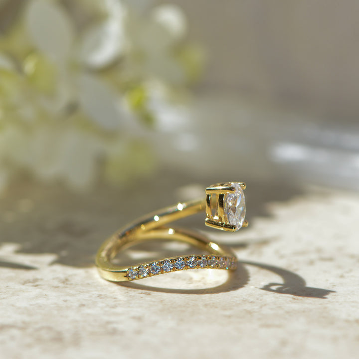 Gold ring with diamond on a textured surface with blurred flowers in the background