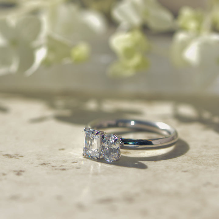Platinum ring with two diamonds on a marble surface with flowers in the background