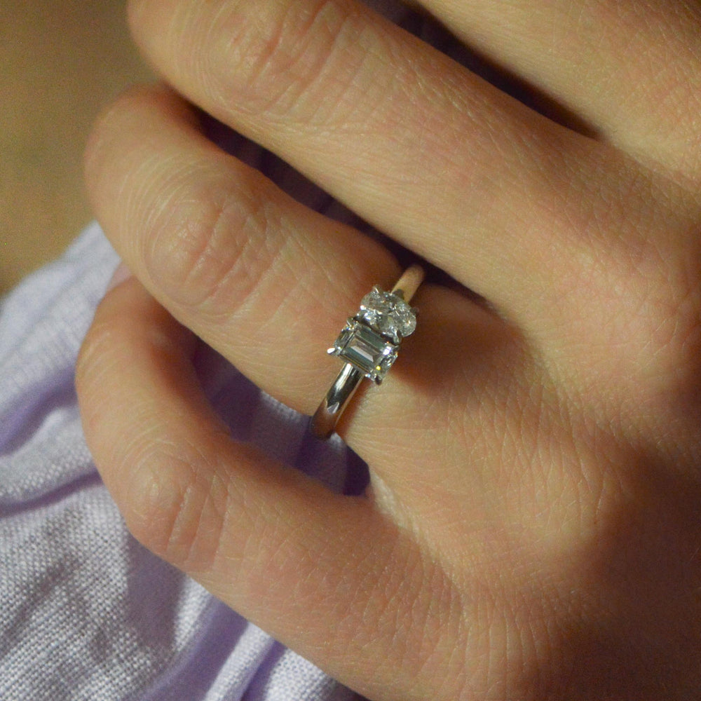Close up of a Toi et Moi ring worn on the hand with an emerald cut and oval cut diamond 