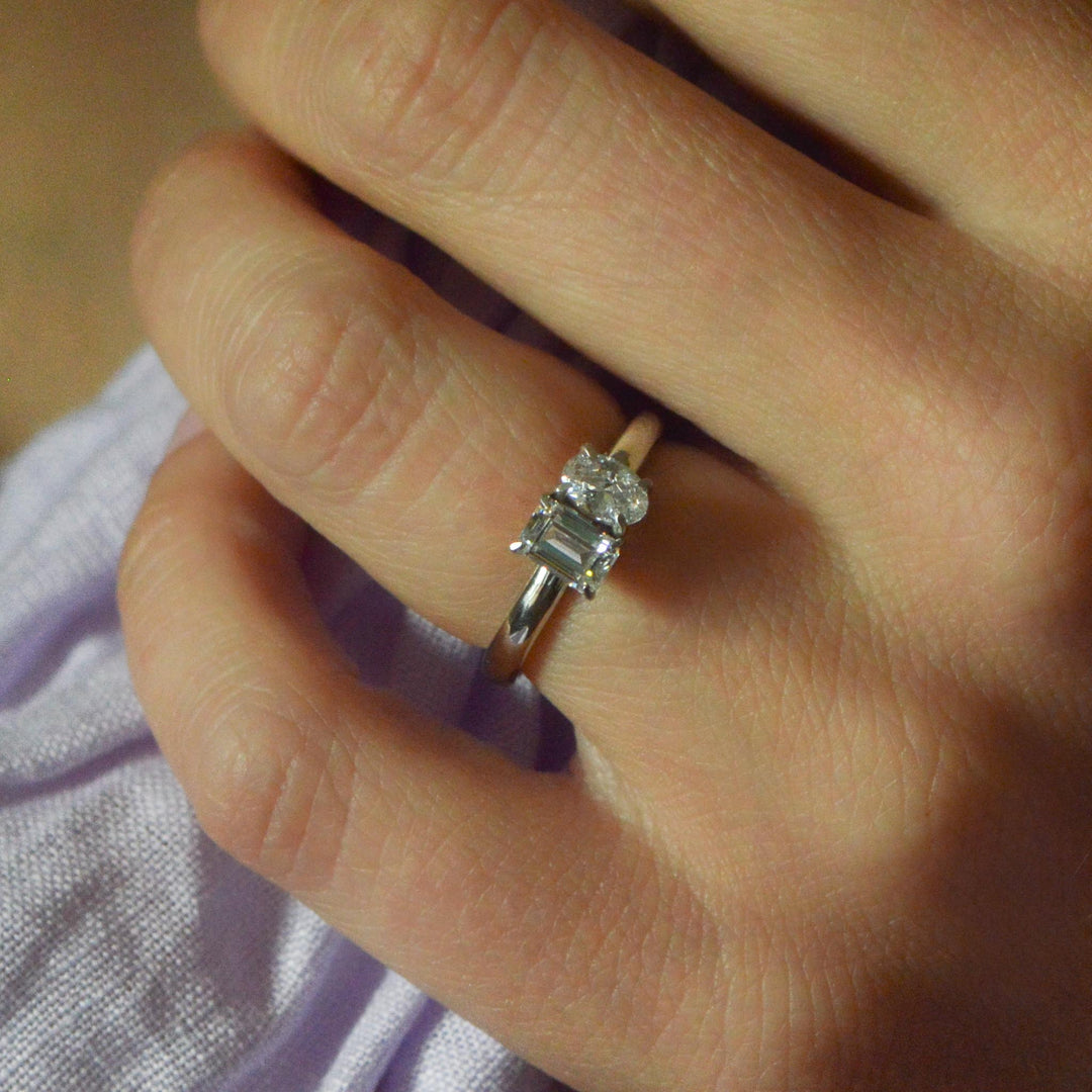 Close up of a Toi et Moi ring worn on the hand with an emerald cut and oval cut diamond 