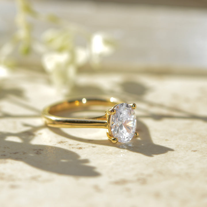 Gold engagement ring with an oval diamond on a light background