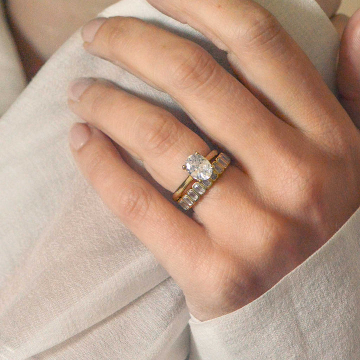 Close-up of a hand wearing two gold rings with diamond accents on a light background