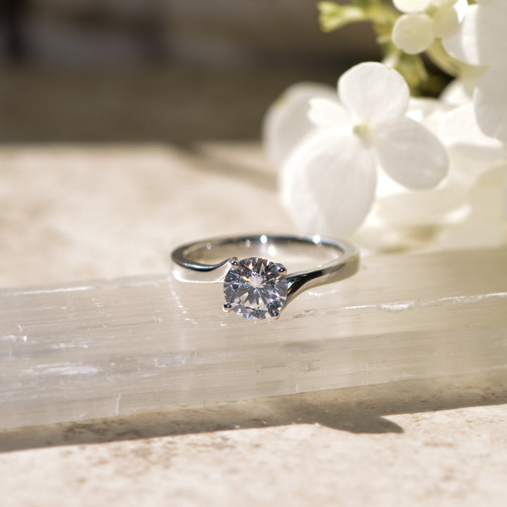 Diamond solitaire ring on marble with white flowers in the background