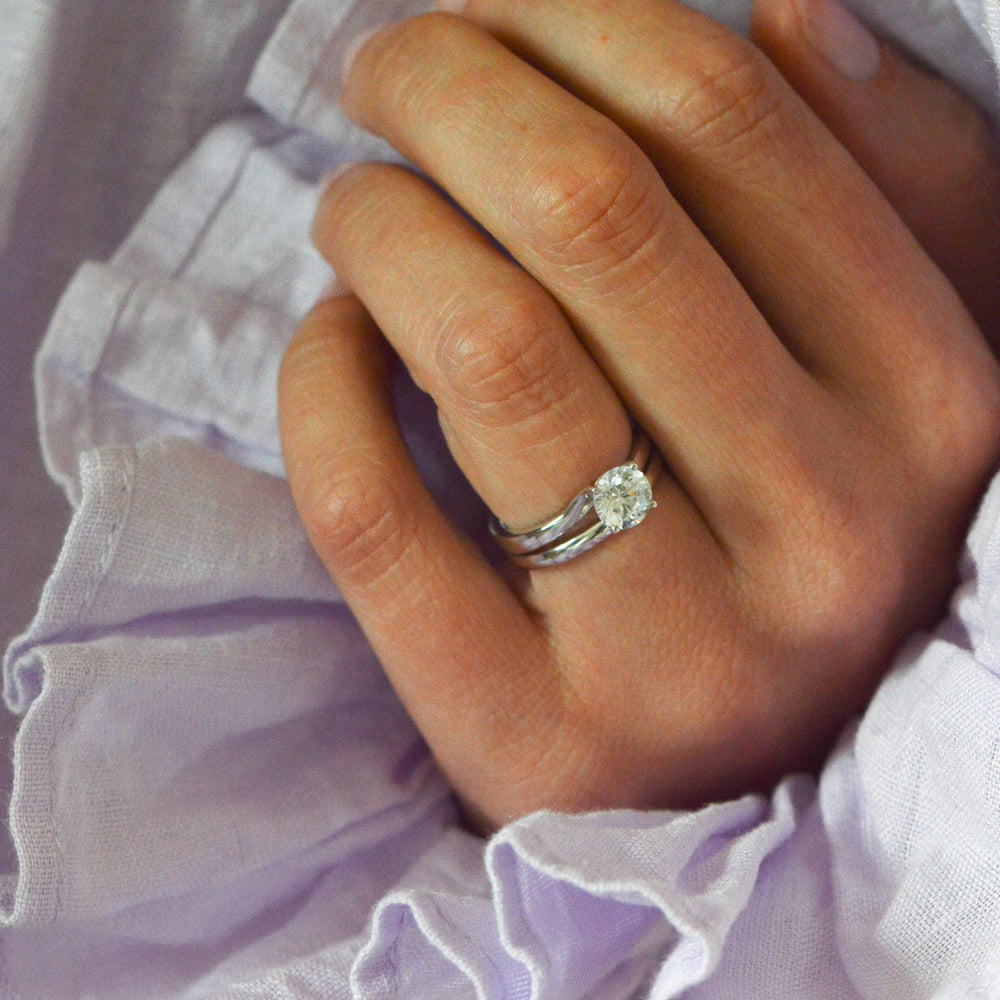 Round cut platinum engagement ring worn on the hand with a classic wedding band
