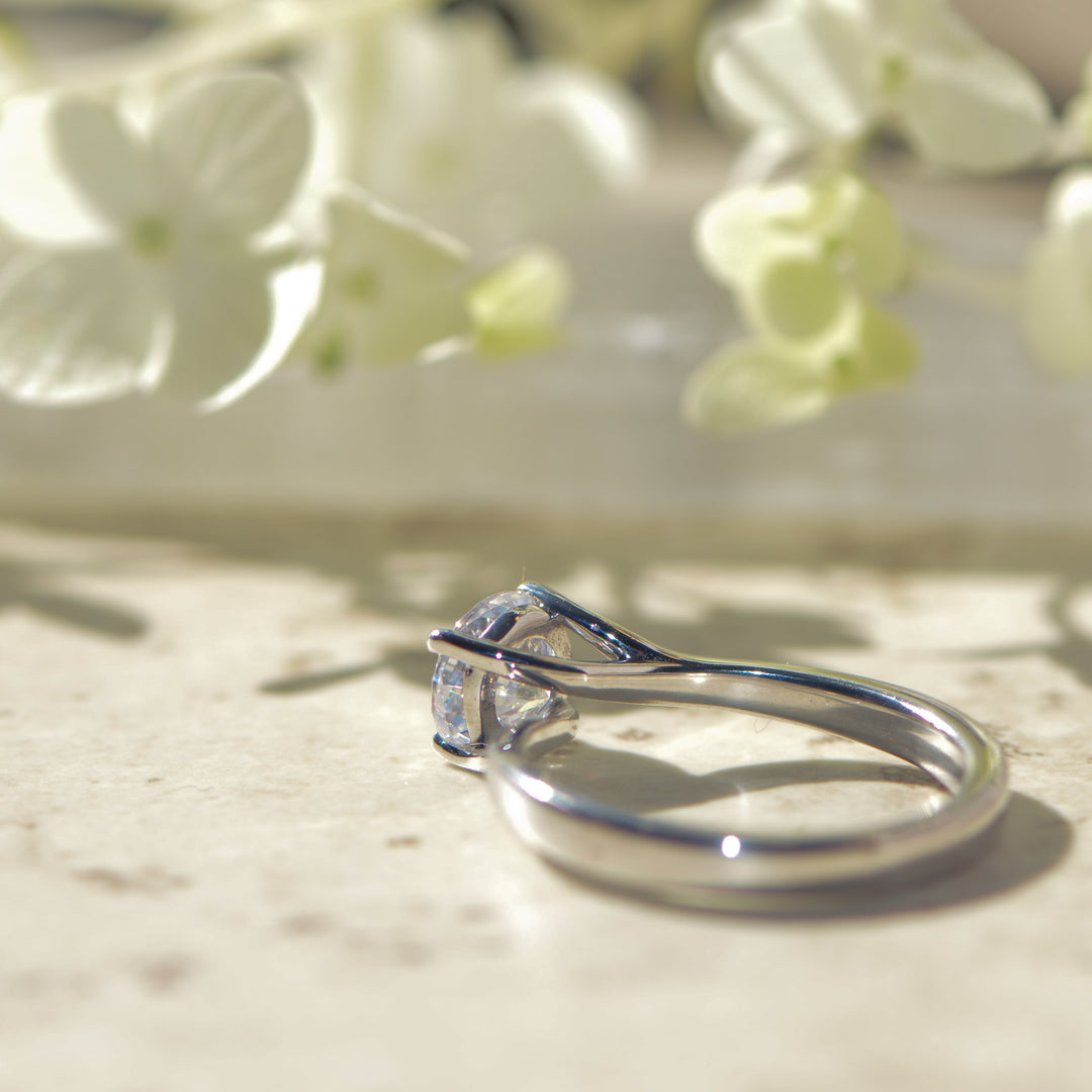 Platinum engagement ring with a twist setting on a light background with flowers