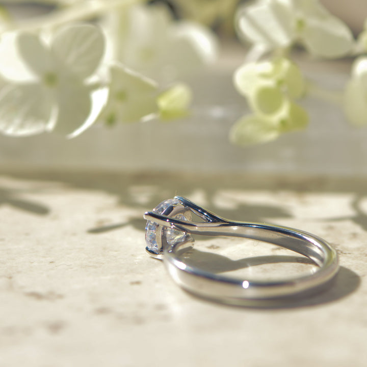 Platinum engagement ring with a twist setting on a light background with flowers