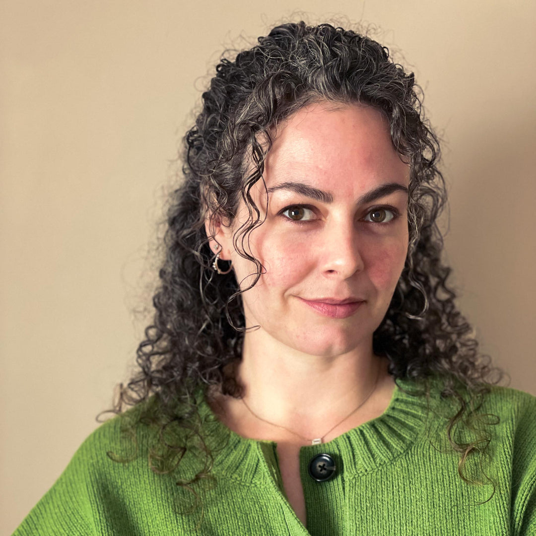 Woman with curly hair wearing a green sweater against a beige background