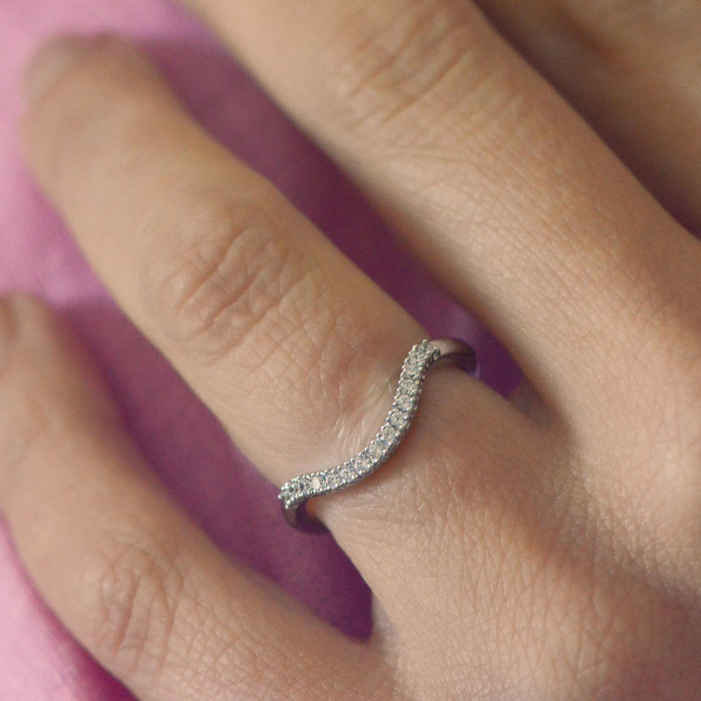 Close up of a curved, diamond pavé set platinum wedding band worn on a finger