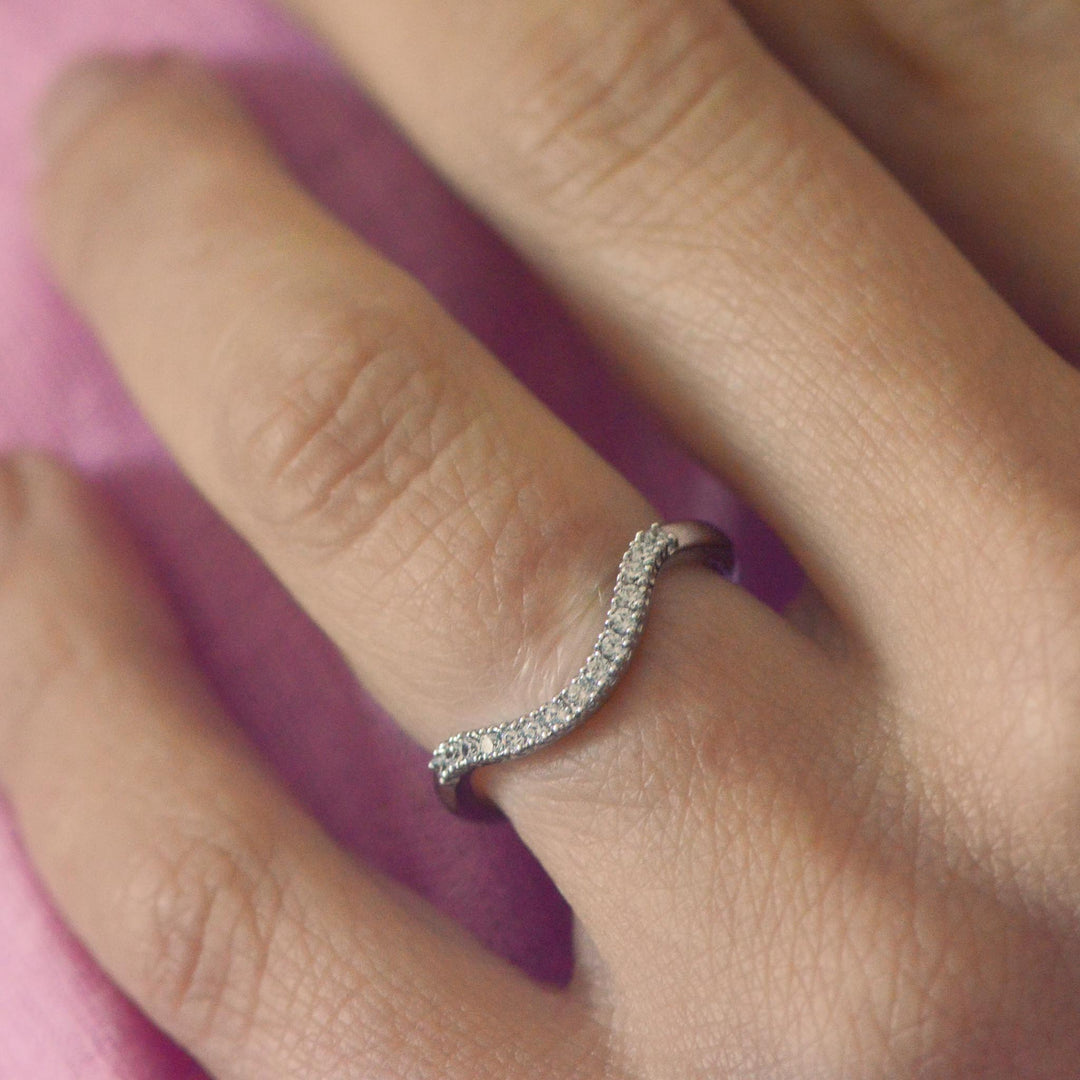 Close up of a curved, diamond pavé set platinum wedding band worn on a finger