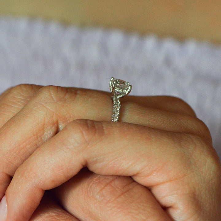 Side profile of a hidden halo shoulder set engagement ring set with diamonds, shown worn on the hand