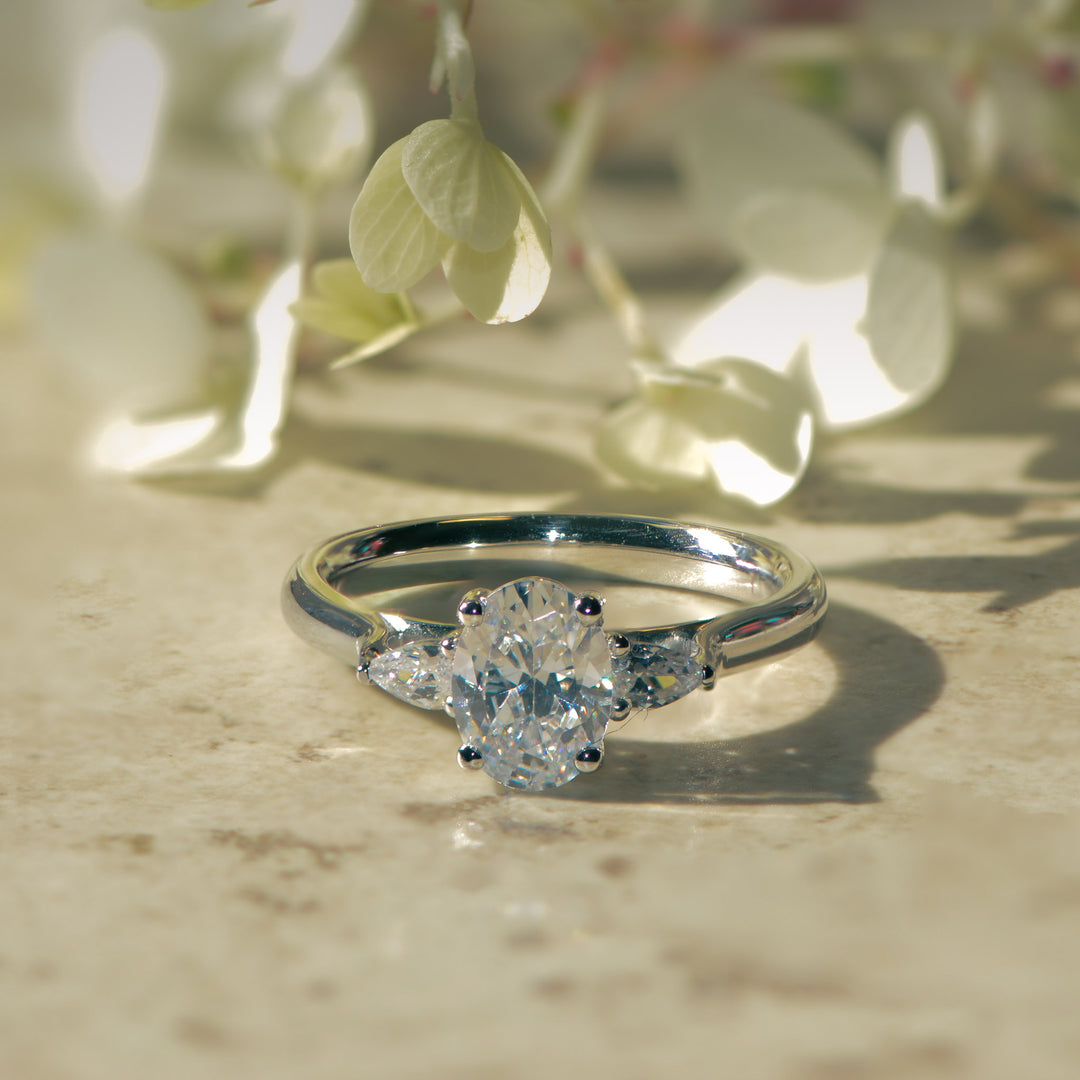 Oval and pear cut three stone diamond  engagement ring on a marble background with blurred flowers in the background