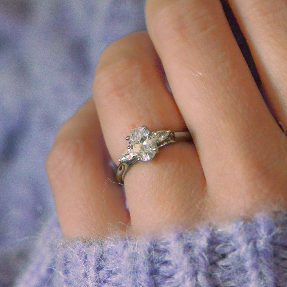 Close-up of a hand wearing a diamond trilogy ring with a blurred purple background