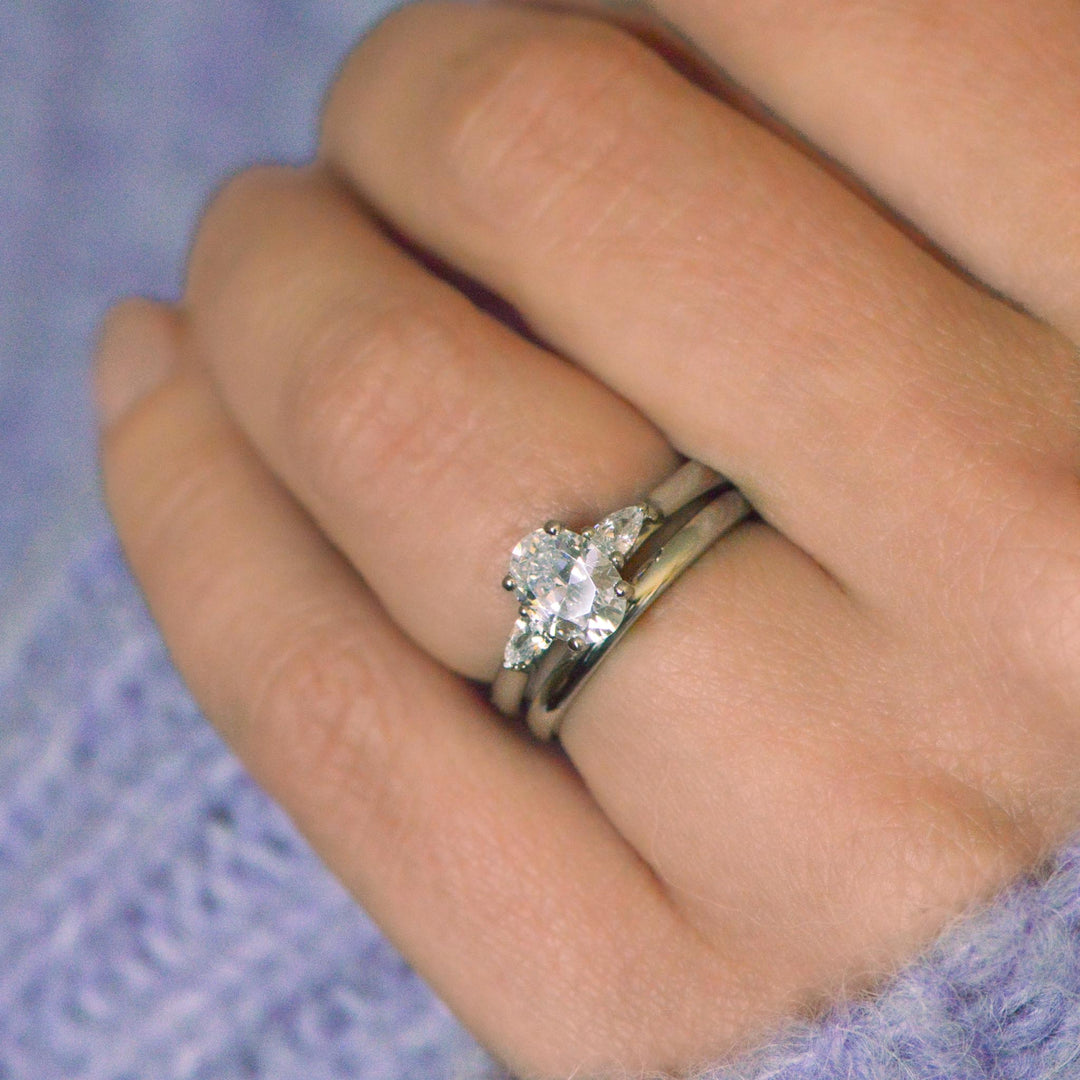 Close-up of a hand wearing a diamond three stone rings with a platinum wedding band on a textured purple fabric background