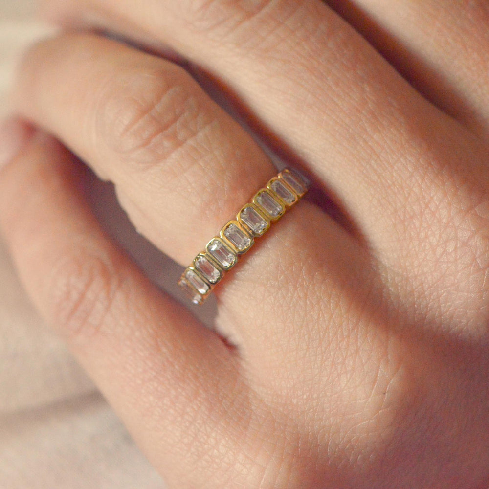 Art deco inspired gold ring with emerald cut diamonds on a person's finger