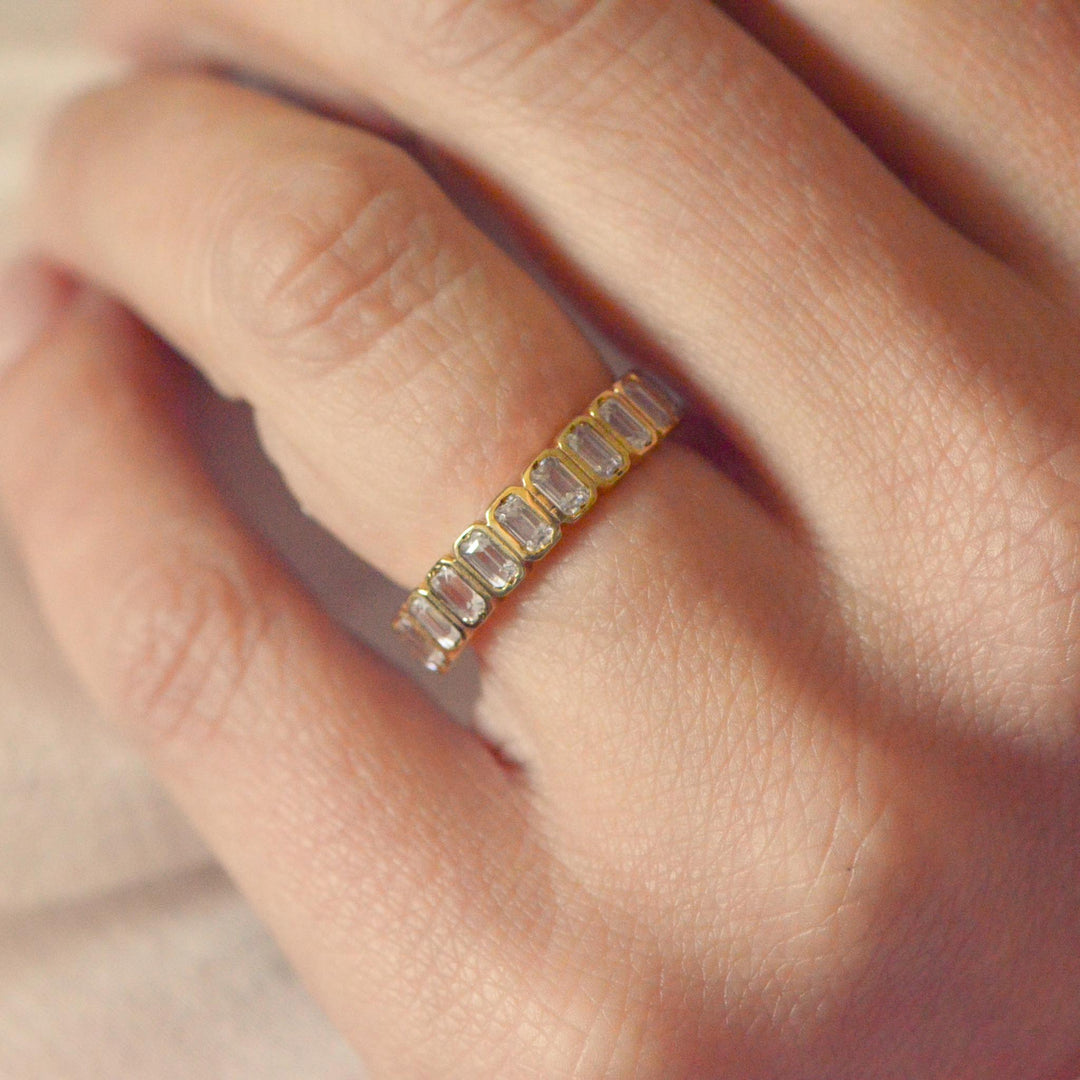 Art deco inspired gold ring with emerald cut diamonds on a person's finger