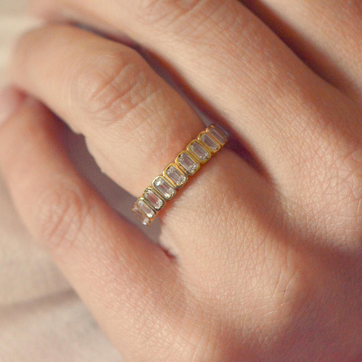 Art deco inspired gold ring with emerald cut diamonds on a person's finger