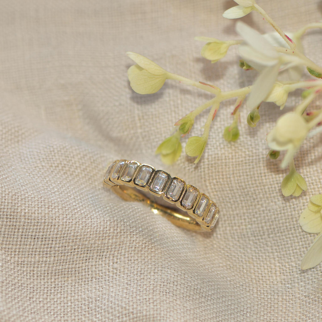 Gold ring with emerald-cut diamonds on a beige fabric background