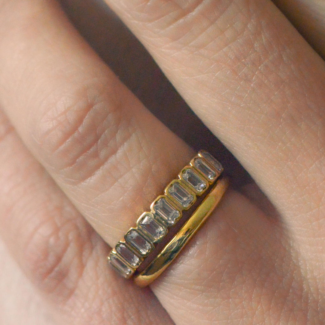 Gold ring with emerald cut diamonds worn with a classic wedding band on a finger