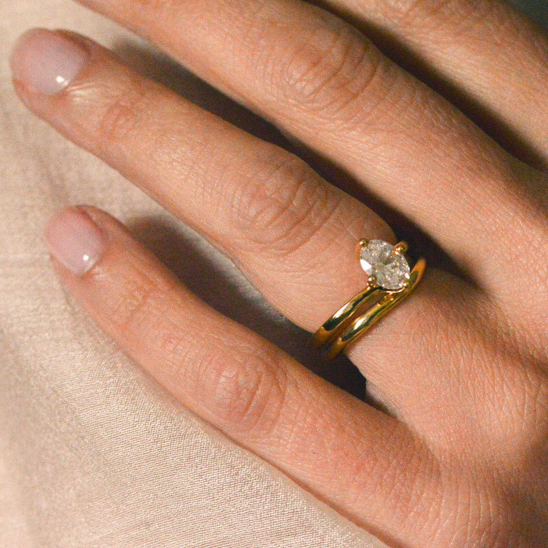 Close cup of an oval diamond solitaire ring worn on the hand with a gold wedding band