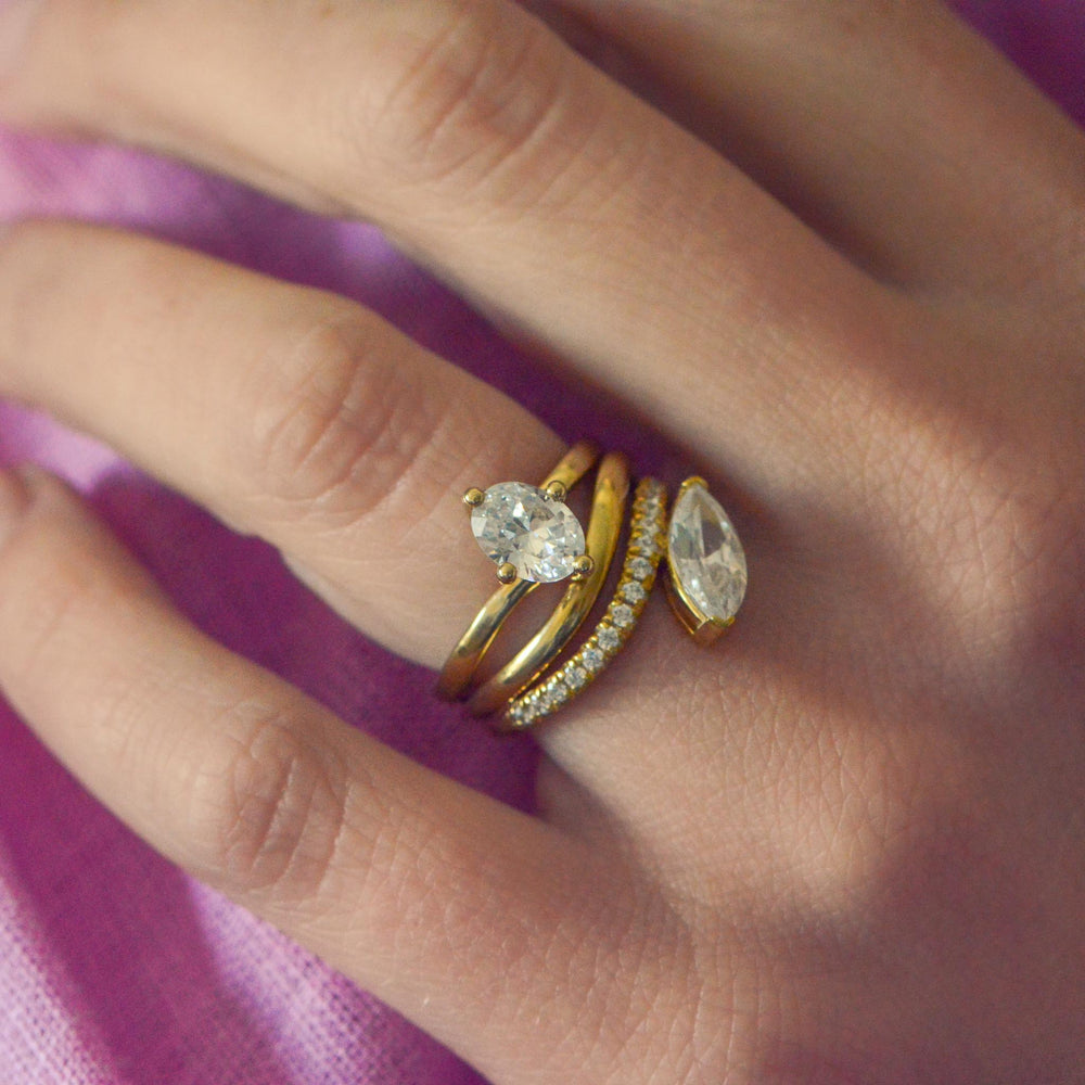 Close-up of a hand wearing two gold rings set with diamonds on a pink fabric background