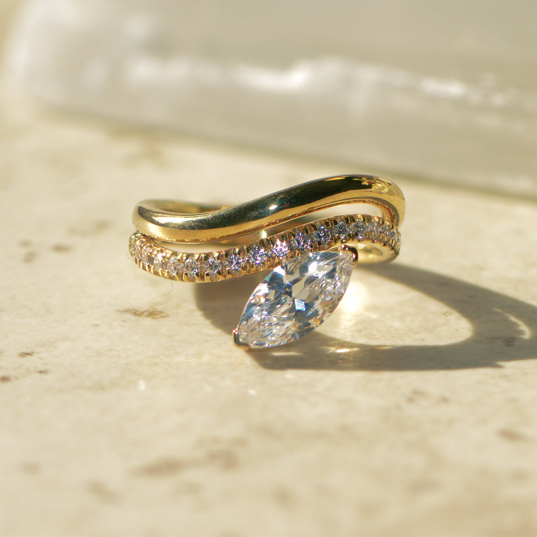 Gold curved engagement ring with a large diamond on a beige surface