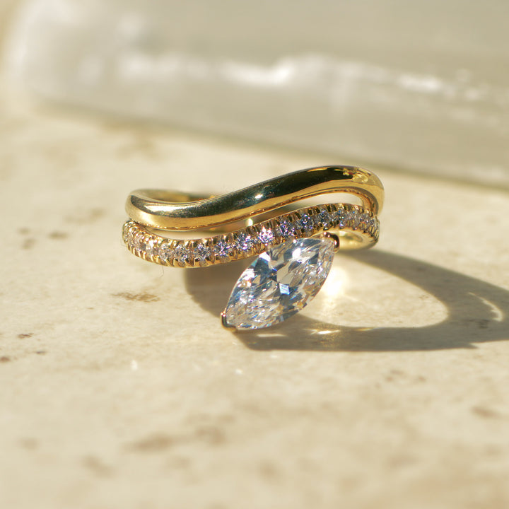 Gold curved engagement ring with a large diamond on a beige surface