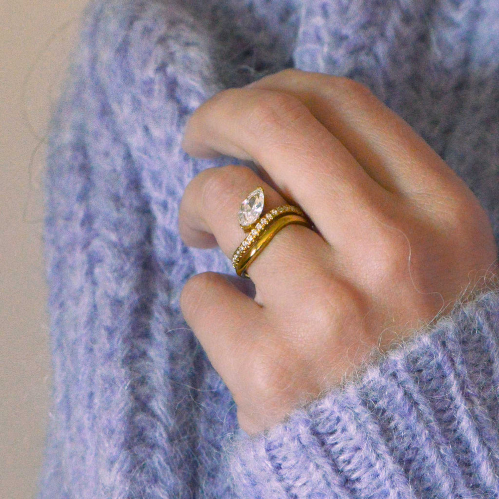 Marquise cut engagement ring on the hand, in gold and set with diamonds. Model wears a lilac wool jumper 