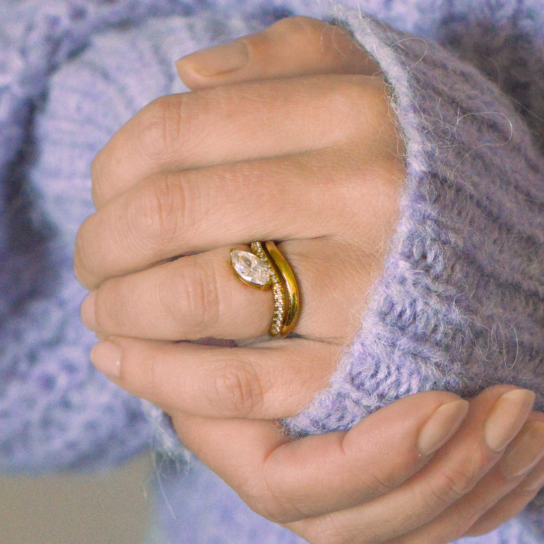 Close-up of a hand wearing a gold double band ring with a blurred purple background