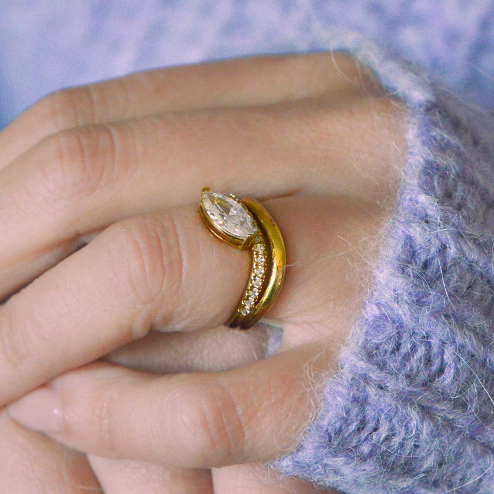 Gold ring with a marquise cut diamond on a finger against a textured purple background