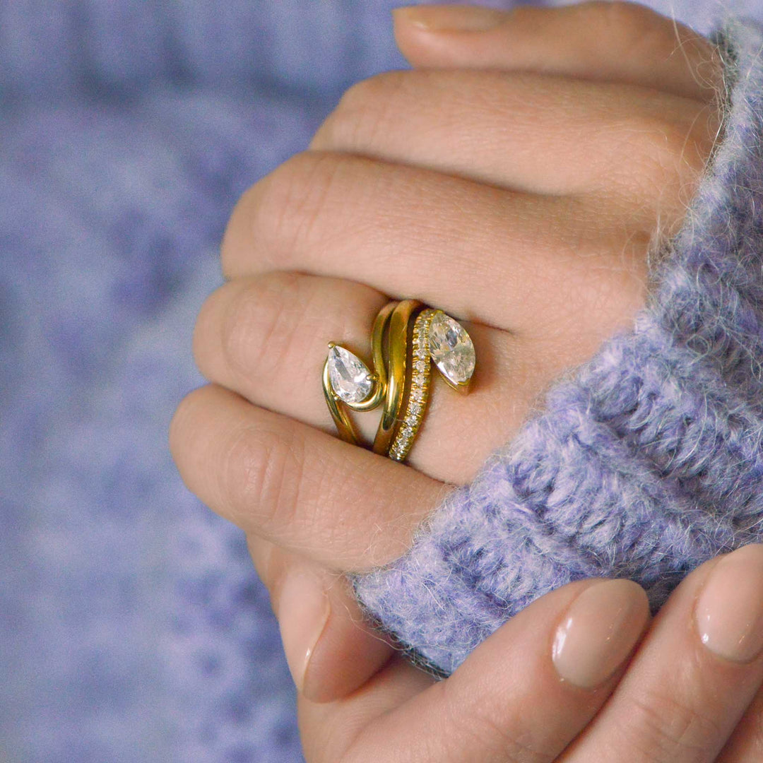 Hand with two contemporary curved diamond rings in gold. Model wears lilac jumper