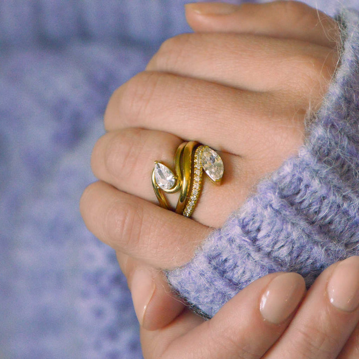 Hand with two contemporary curved diamond rings in gold. Model wears lilac jumper