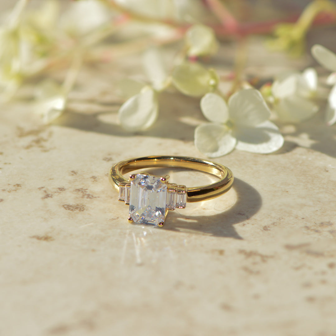 Gold  art deco ring with a diamond on a marble surface with flowers in the background