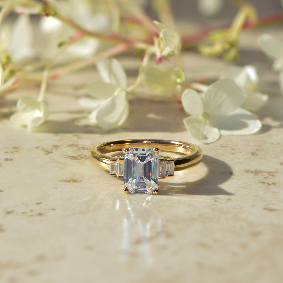 Emerald cut art deco inspired diamond ring on a Mable surface with flowers in the background