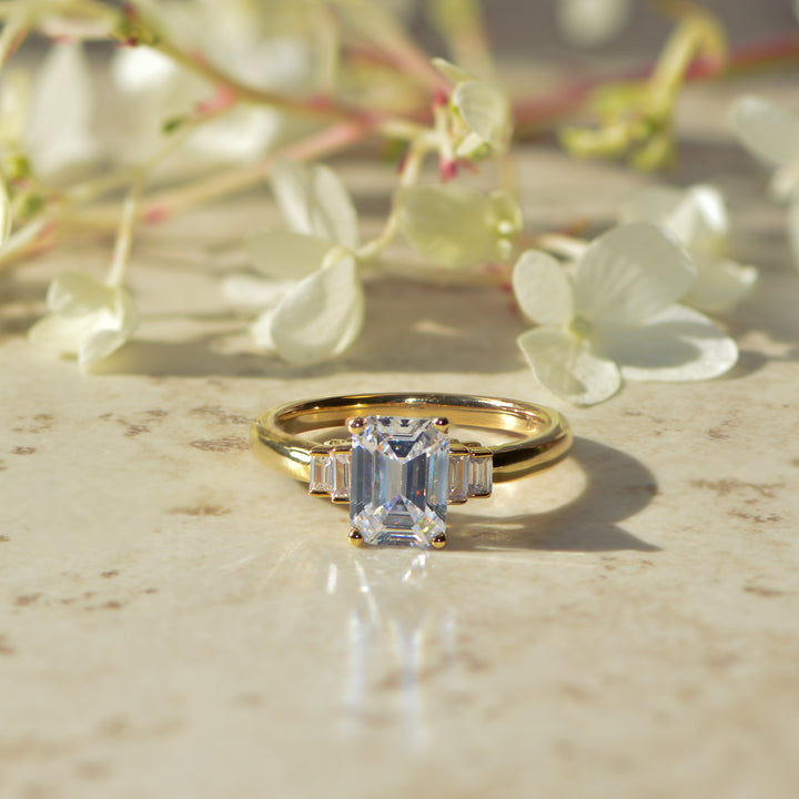 Emerald cut art deco inspired diamond ring on a Mable surface with flowers in the background
