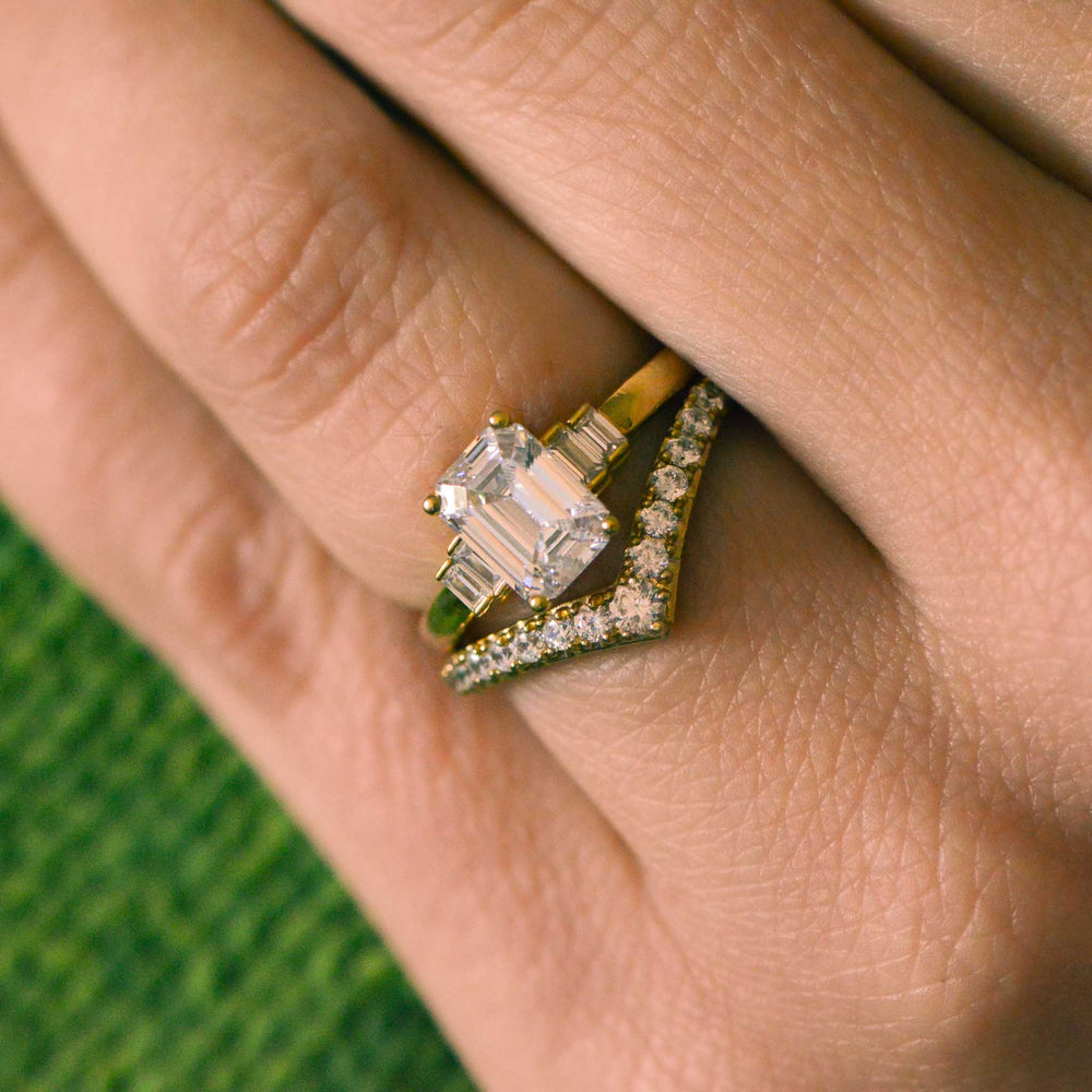 Gold ring with a large diamond on a finger against a green fabric background