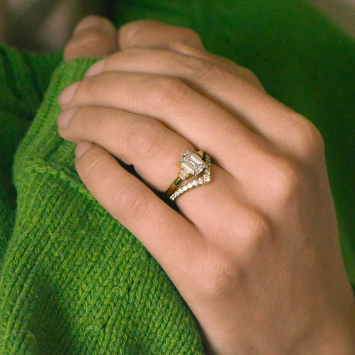 Hand wearing a diamond and gold engagement ring on a green sweater