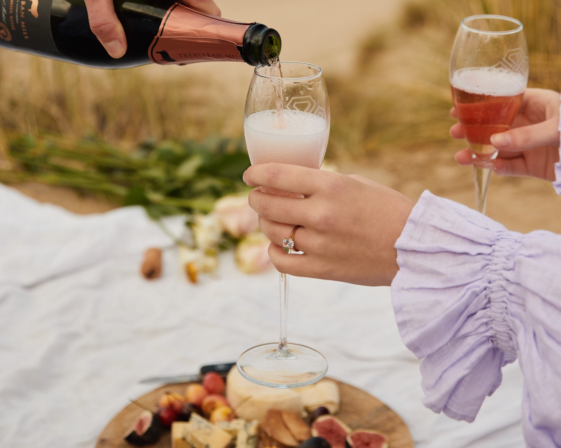 Person pouring champagne into a glass at an outdoor picnic setting.