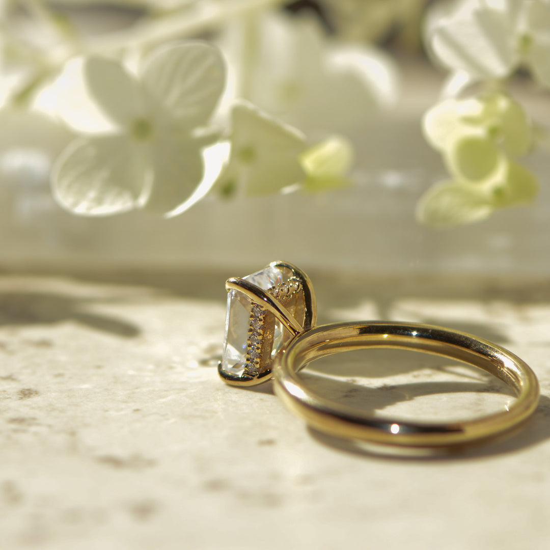 Gold ring with a diamond hidden halo on a marble surface with white flowers in the background