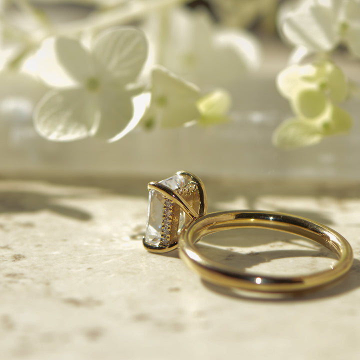 Gold ring with a diamond hidden halo on a marble surface with white flowers in the background