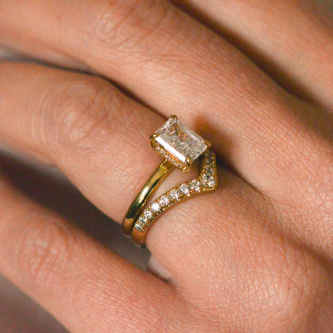 Side view of a hidden halo radiant cut diamond ring worn on the hand with a pavé set wedding band 