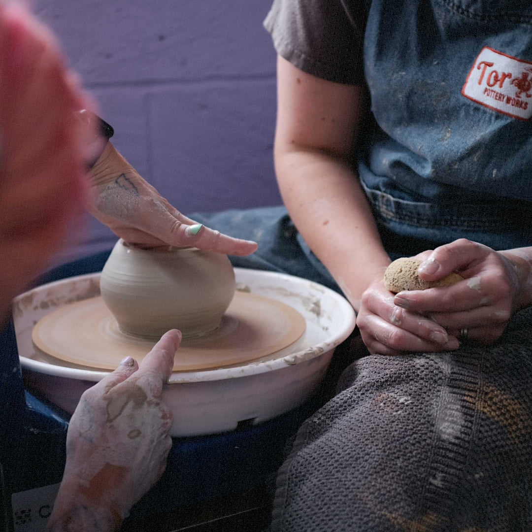 Two people working together with clay on a pottery wheel during a ceramic workshop in Cornwall. 