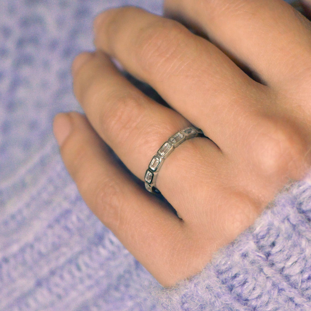 Hand wearing a art deco inspired wedding ring on a textured purple fabric background