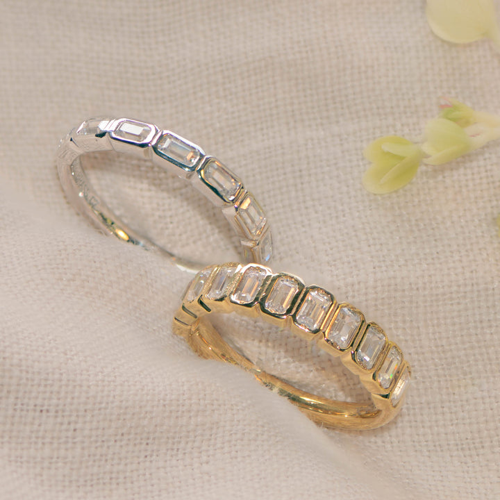 Two rings set with emerald cut diamonds, one in gold and one in platinum, on a beige linen background