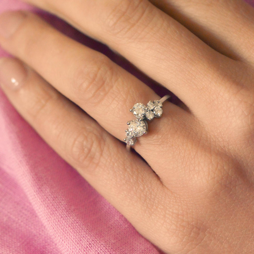 Platinum ring with a cluster of round diamonds on a hand against a pink fabric background